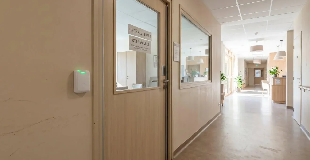 Porte d'entrée sécurisée d'une unité protégée Alzheimer avec système de badge électronique visible, couloir lumineux moderne au-delà